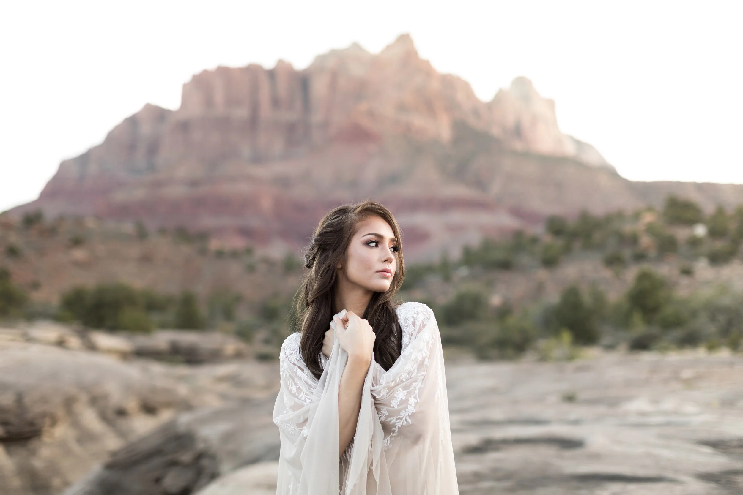 Woman in white dress posing in front of rugged mountain landscape.